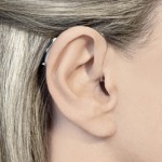 小型の耳掛け型補聴器を付けている写真